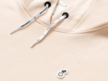 Beige women’s golf hoodie close-up with drawstring hood and minimalist logo detail.